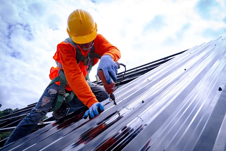 worker installing metal roofing with drill