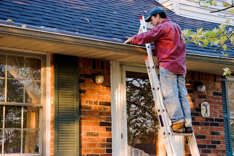 man standing on ladder cleaning out gutters