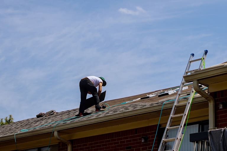 worker replacing a shingle roof