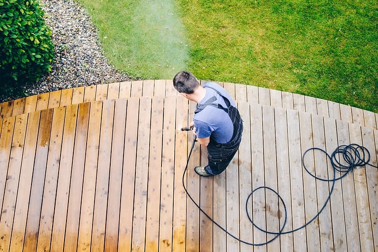 cleaning wood deck surfaces by power washing, revealing a striking contrast between cleaned and uncleaned areas