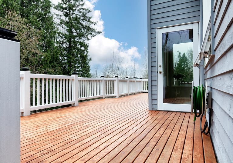Freshly stain large home walk out cedar wood deck patio with trees and sky in background