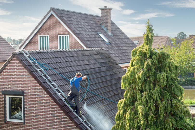 roof coating-roof tech on a roof ladder spraying roof shingles