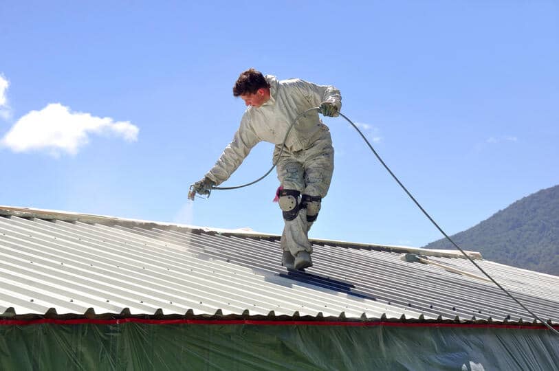 roof coating-tech in a white protective suit spraying liquid onto a metal roof