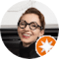 Smiling person with short hair and black glasses, viewed in a circular frame, with an orange star badge in the corner.