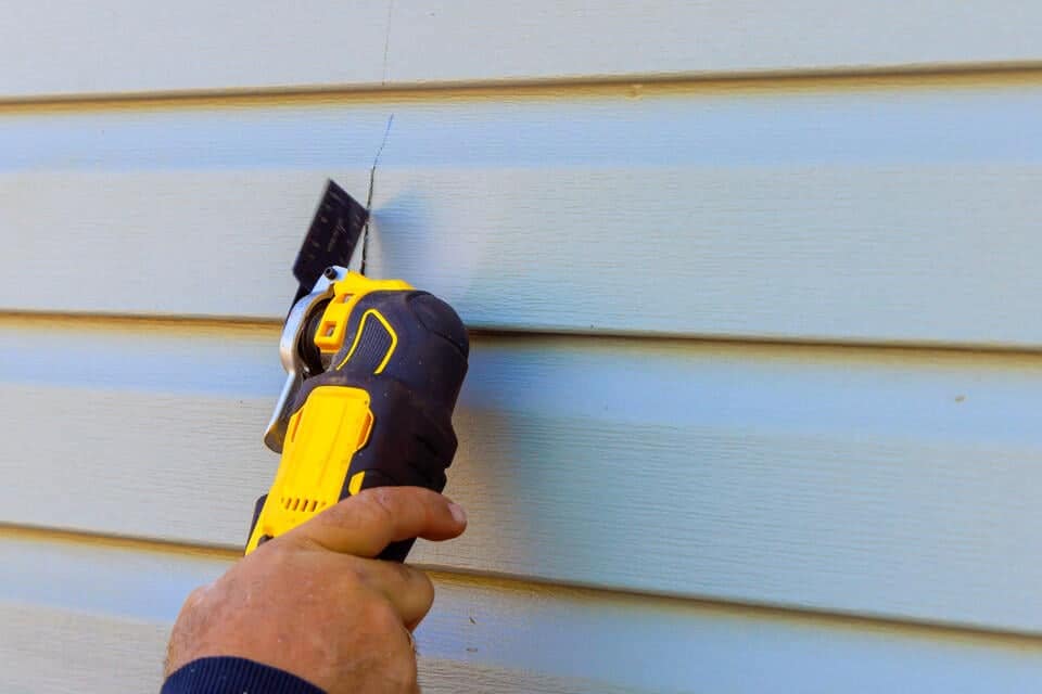 how much does siding replacement cost-man using tool to cut siding materials