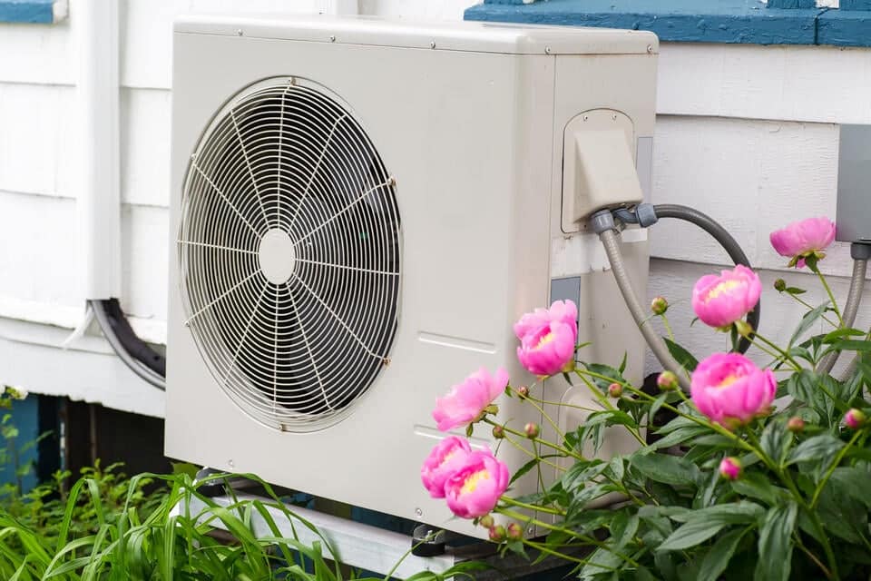 heat-pump-replacement-white-heat-pump-near-house-siding-and-surrounded-by-flowers