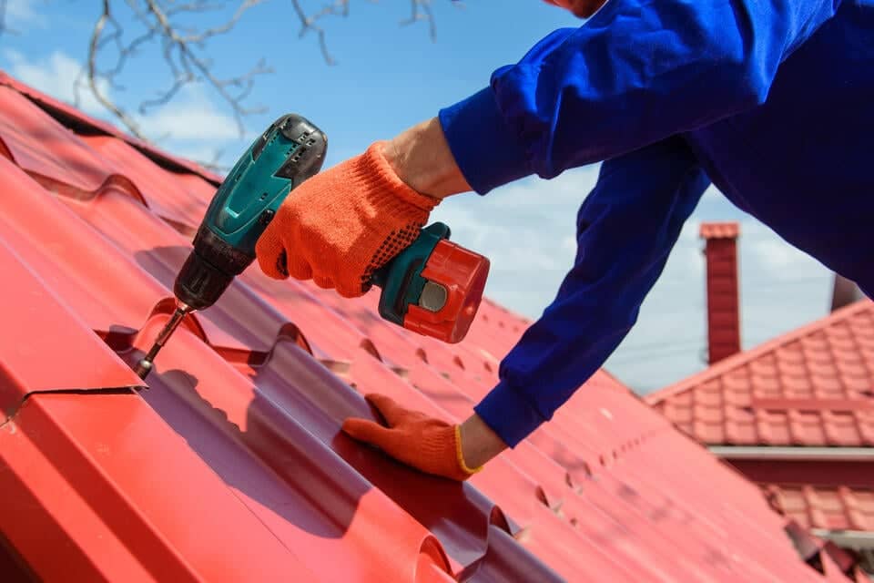 metal roof cost-close up of roofer installing red metal shingles on house roof
