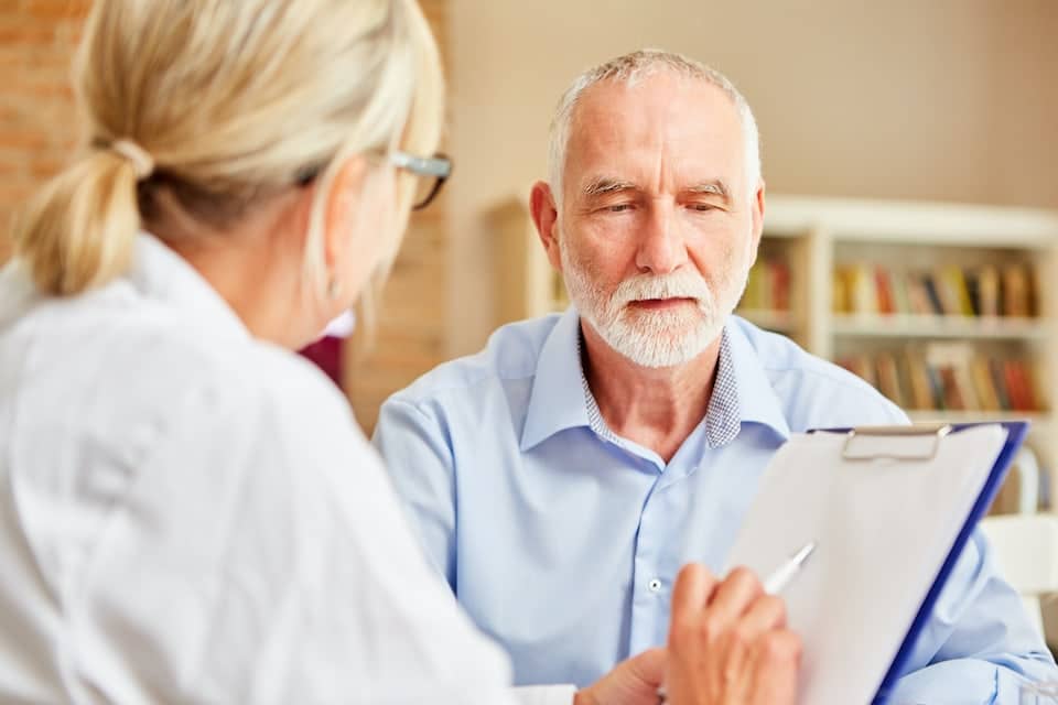 Female doctor sitting and talking with elderly male patient; dealing with dementia