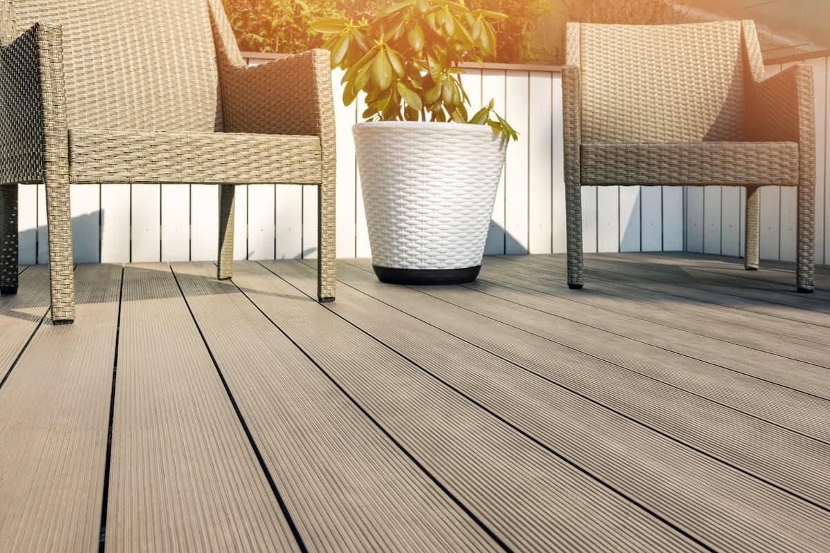 Two wicker chairs sit on a composite deck next to a large white planter with a green leafy plant