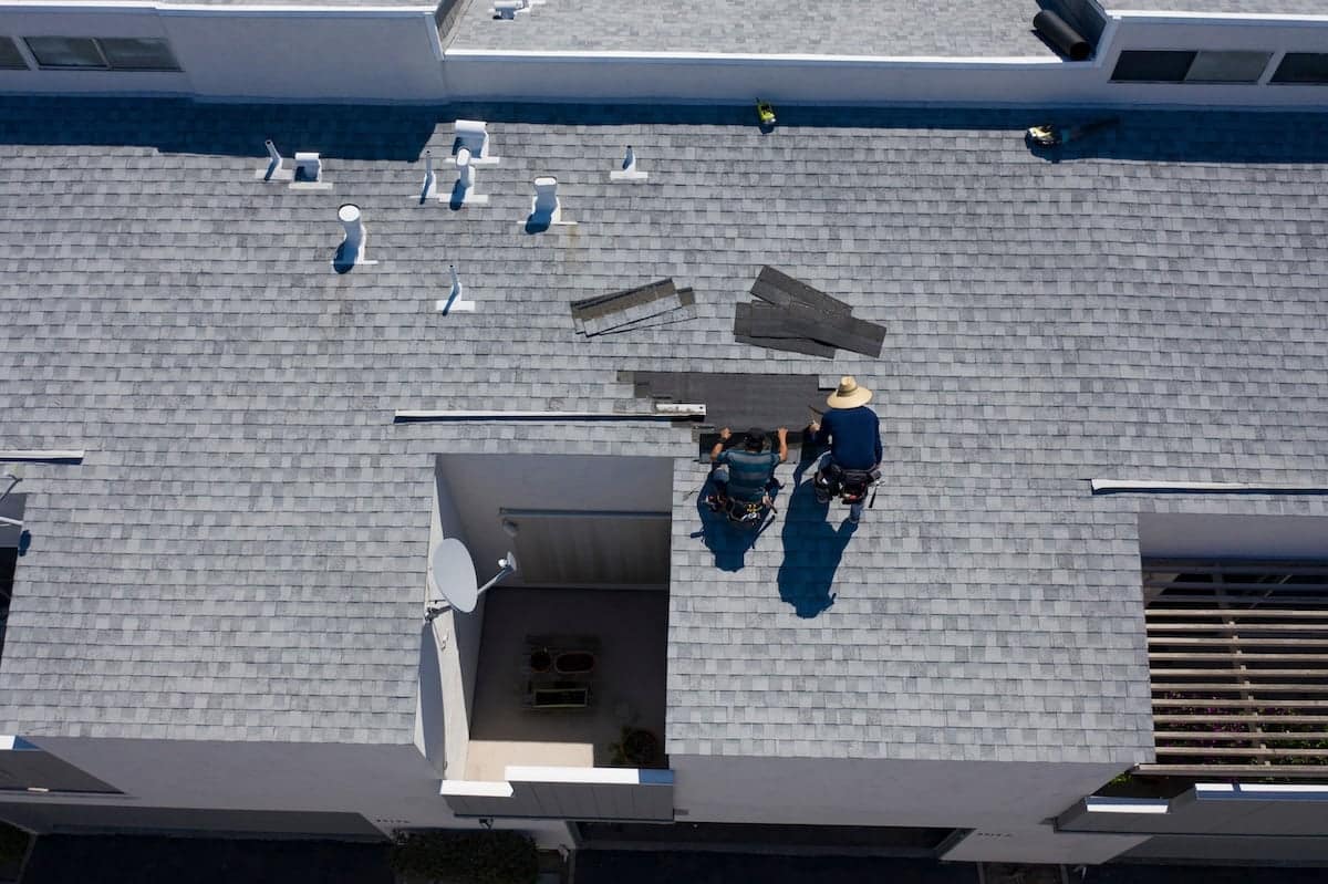 Aerial view of two people working on a grey shingled rooftop.