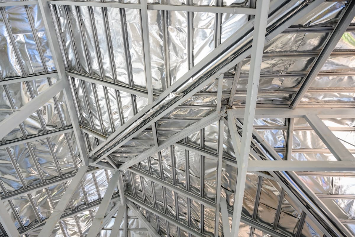 View of an intricate structure of roof beams covered in shiny, silver insulation material