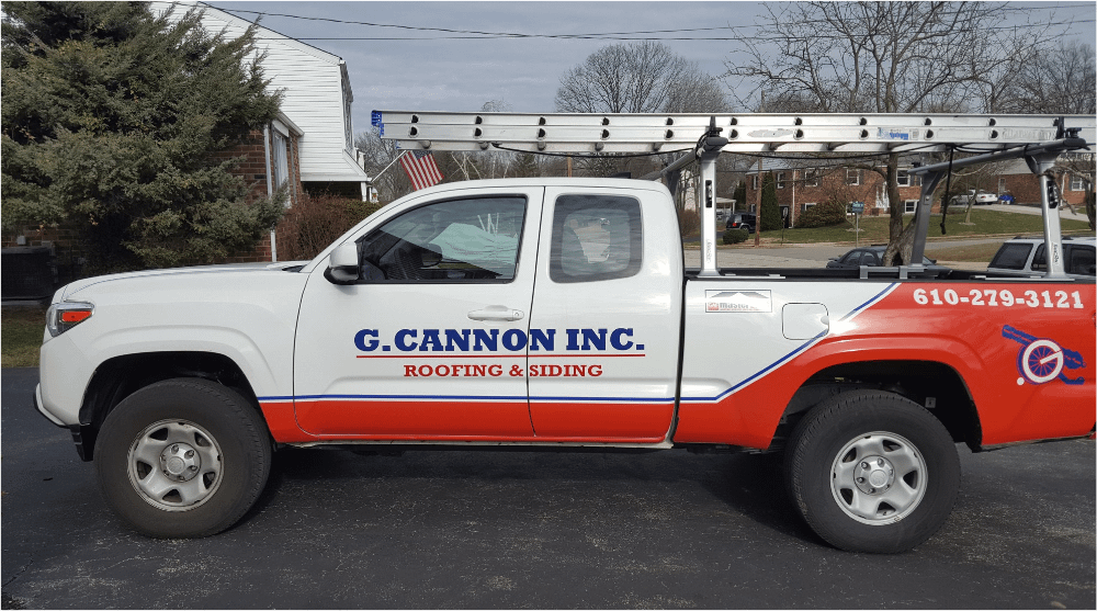 A white and red pickup truck with ladders on top, displaying the logo and contact information for "G. Cannon Inc. Roofing & Siding." The background shows a suburban neighborhood with trees and houses.