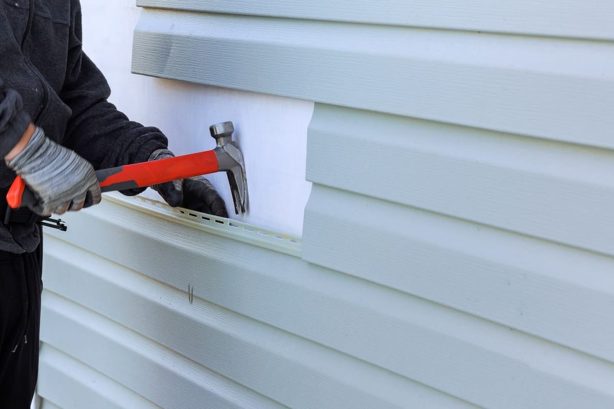 Worker using a hammer to remove vinyl siding