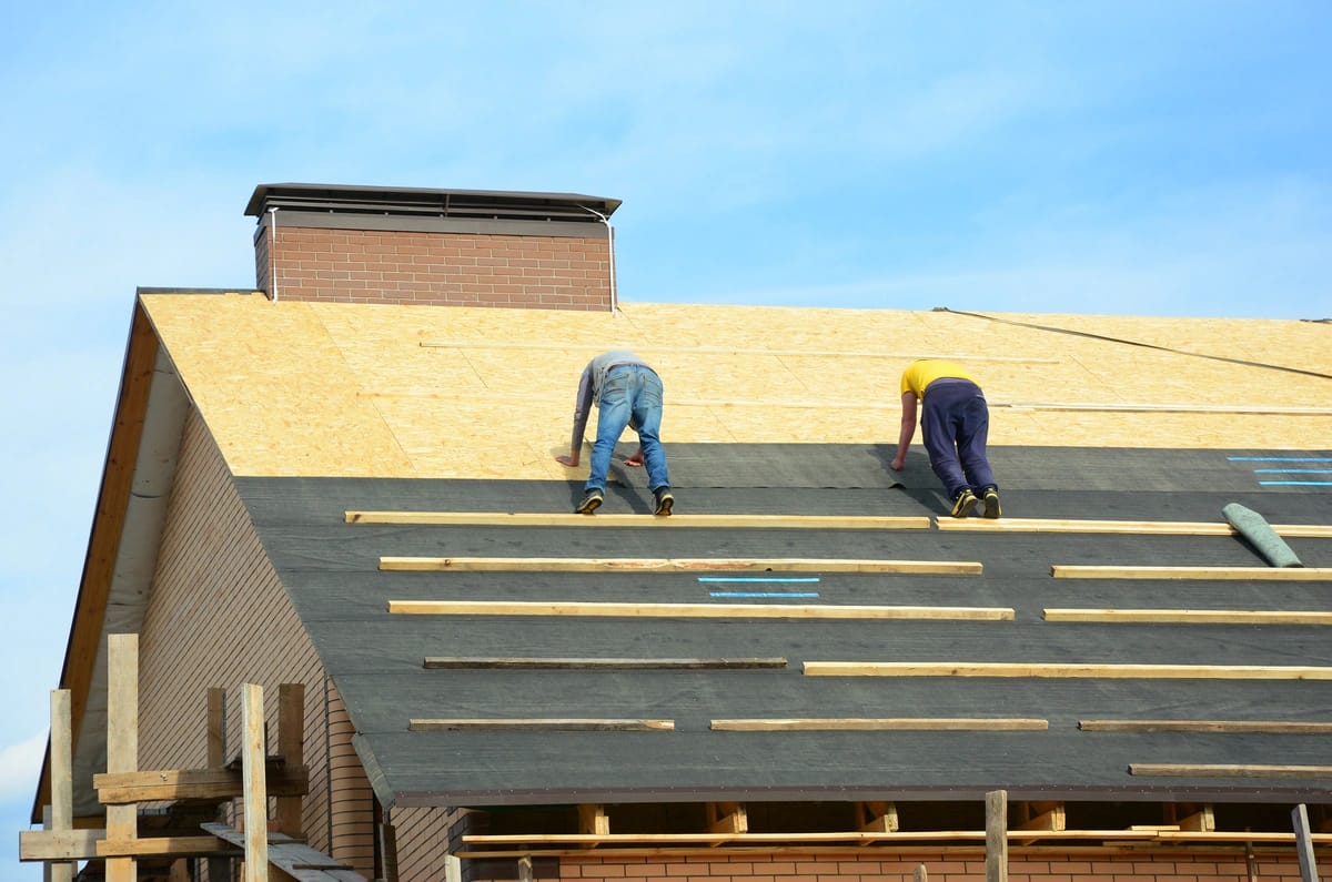 workers on the plywood of the house roof 