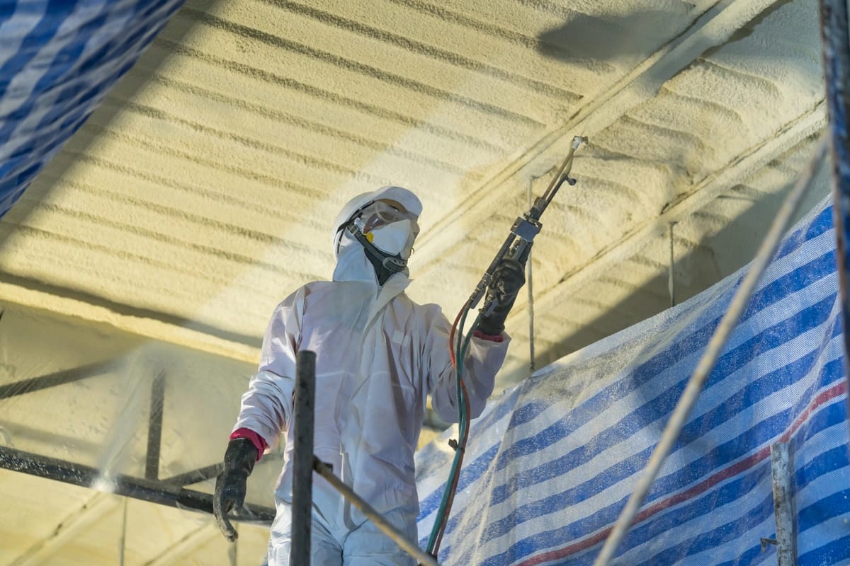 worker wearing suit while foam insulating roof